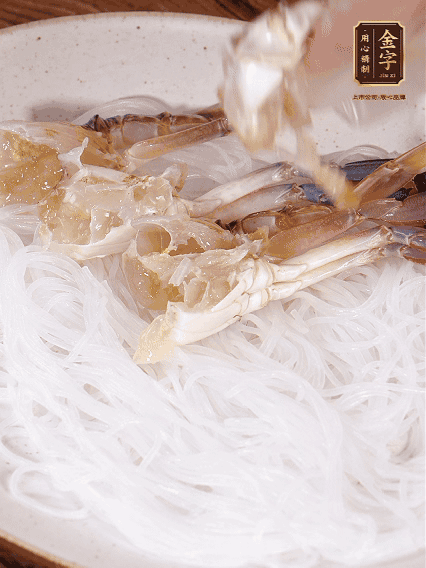 盤底墊上粉絲，擺上梭子蟹、火腿片，撒姜粒，淋上蒸魚豉油、花雕酒調(diào)味腌制15分鐘